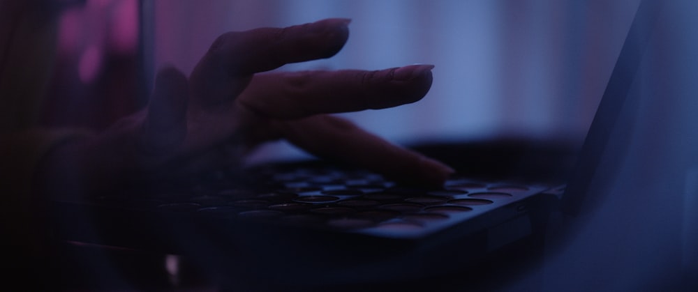 una persona che digita sulla tastiera di un laptop in una stanza buia