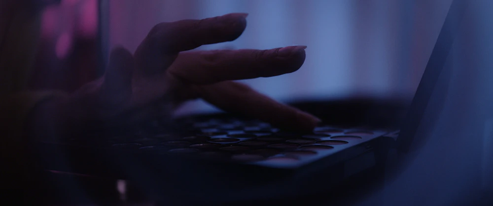 A person using a laptop in a dimly lit room, representing a browser wallet session