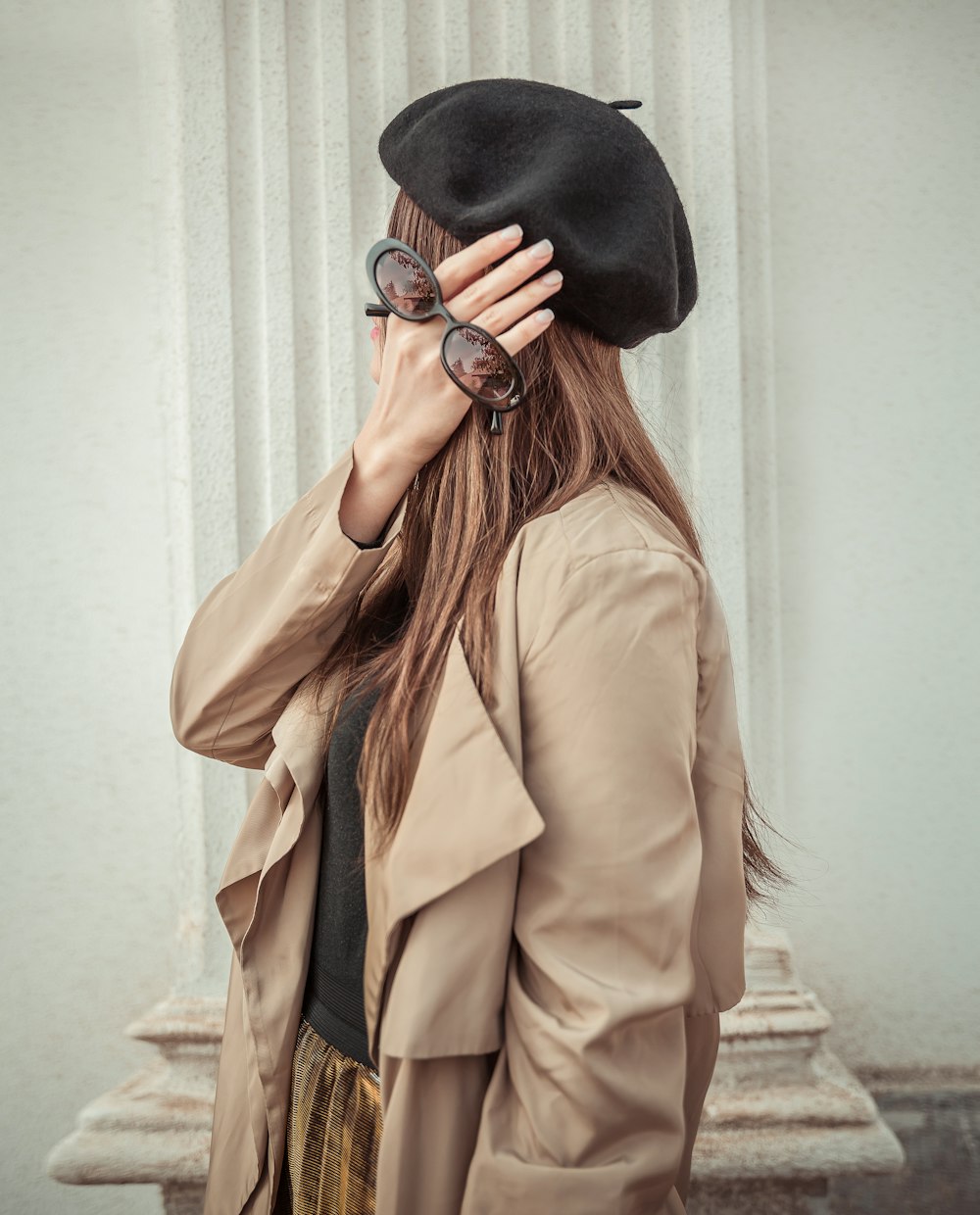 a woman in a trench coat and hat covering her eyes