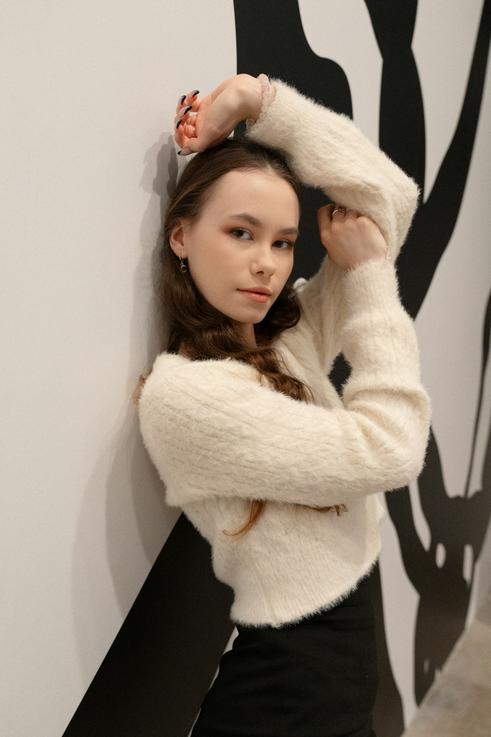 a woman leaning against a wall with her hands on her head