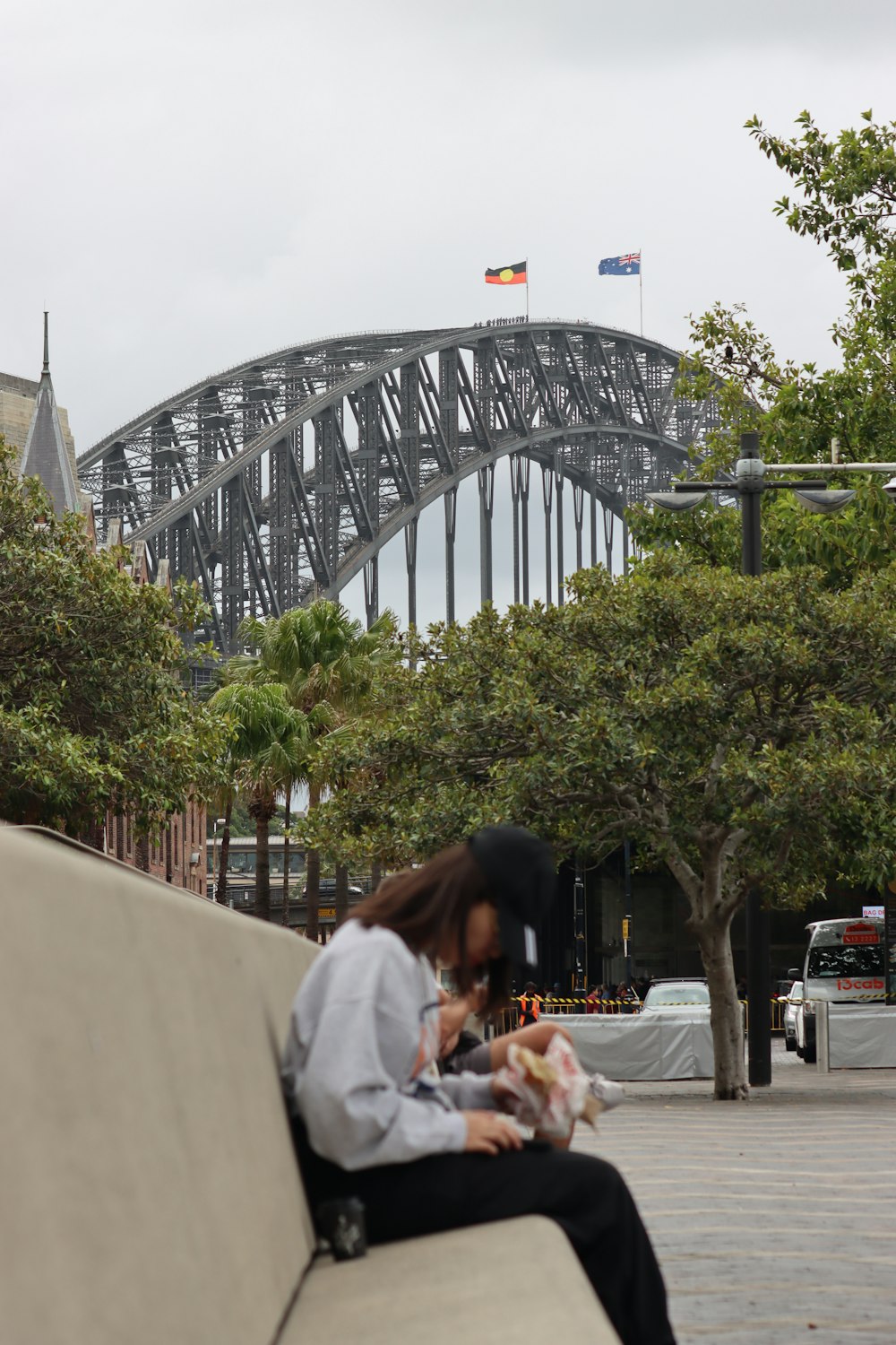 a woman sitting on a bench in front of a bridge