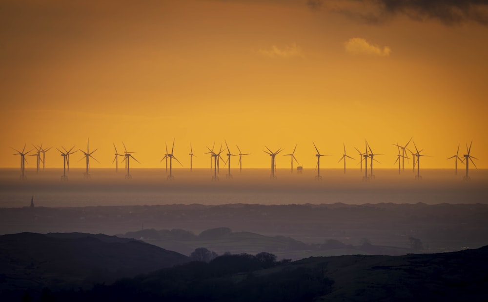 un groupe de moulins à vent sur une colline au coucher du soleil
