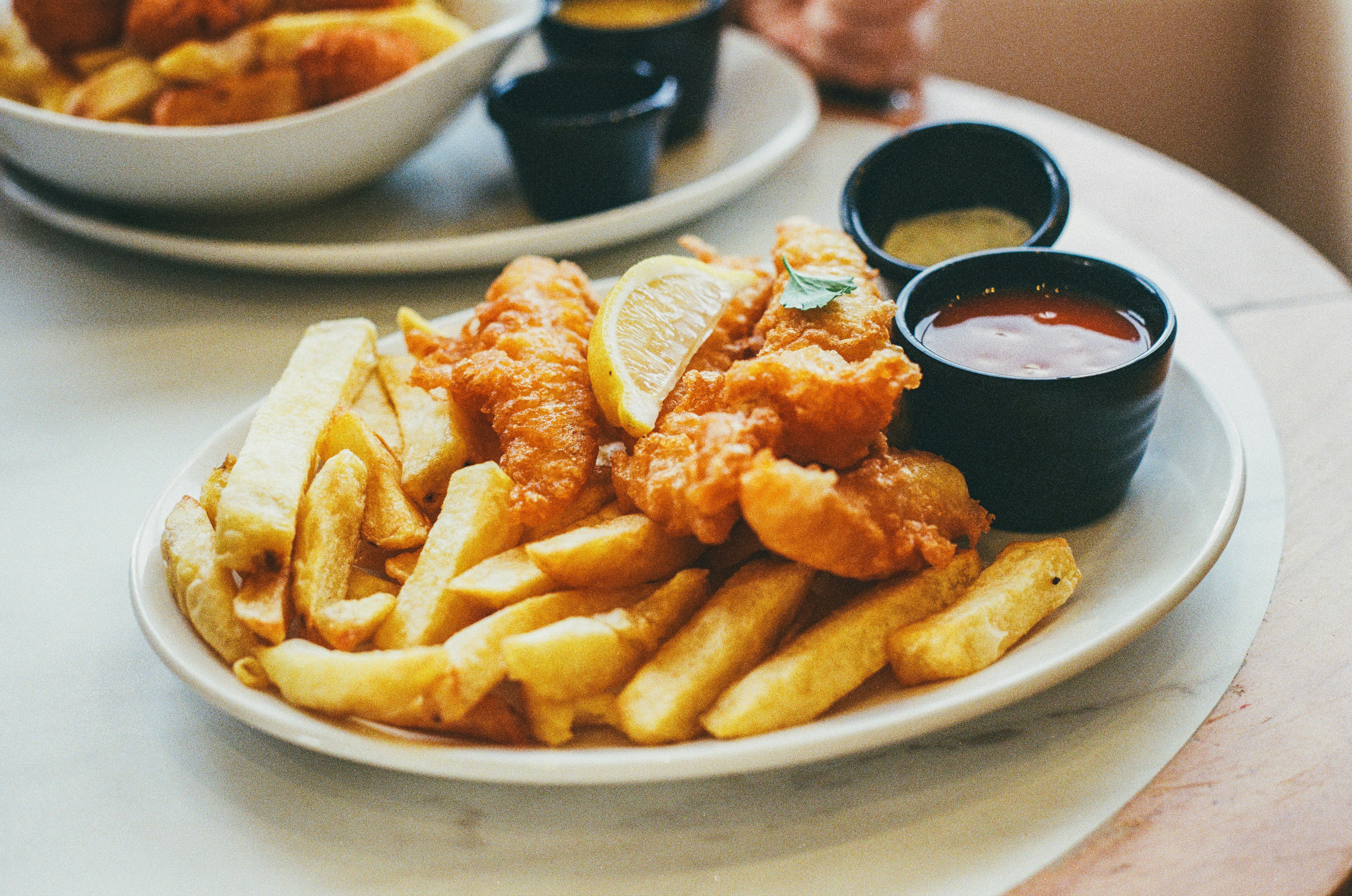 This photo shows traditional fish and chips on a white oval plate garnished with parsley and a lemon wedge