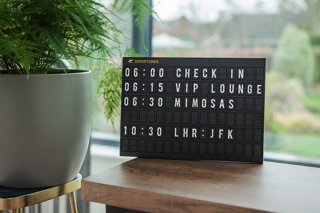 a sign on a table next to a potted plant, Black locomocean board showing departure time for a flight from London to New 