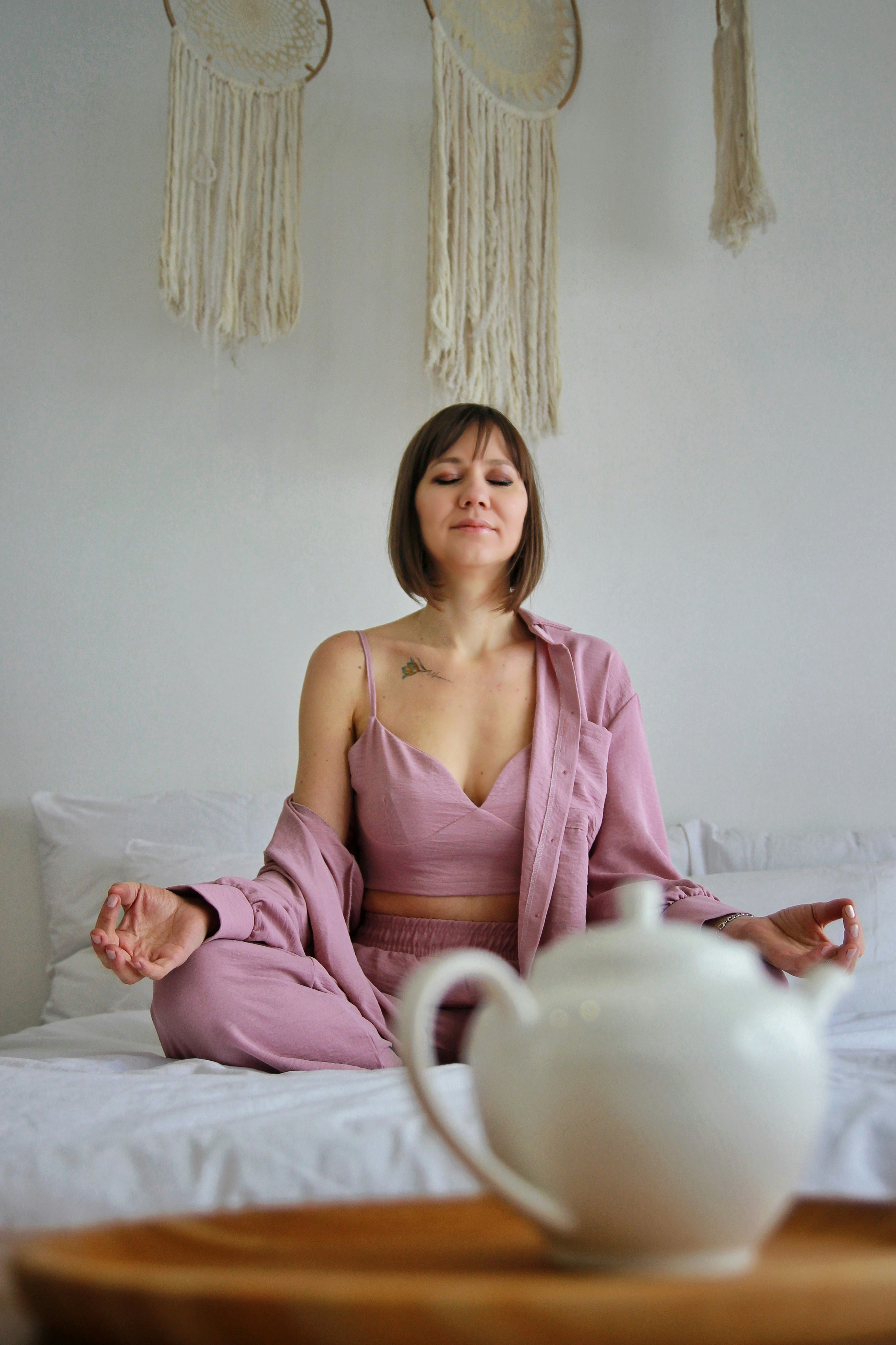 a woman sitting on a bed with a teapot in front of her