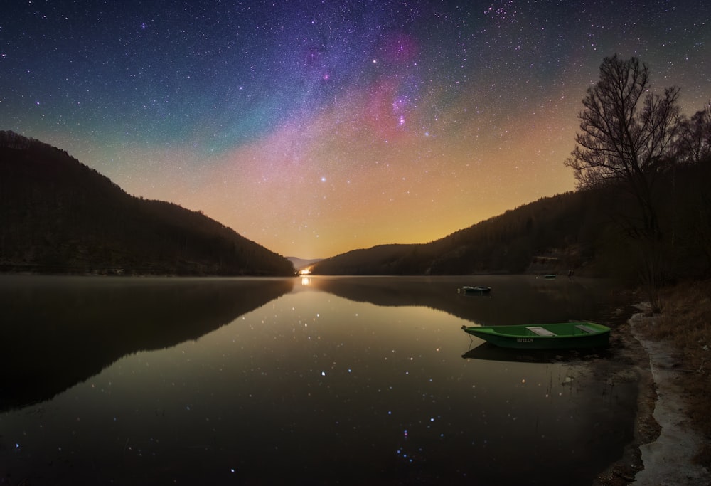 a green boat sitting on top of a lake under a night sky
