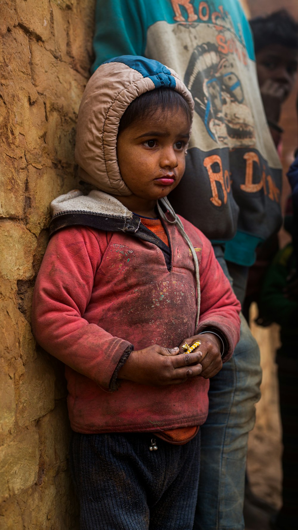 a young boy standing next to a stone wall