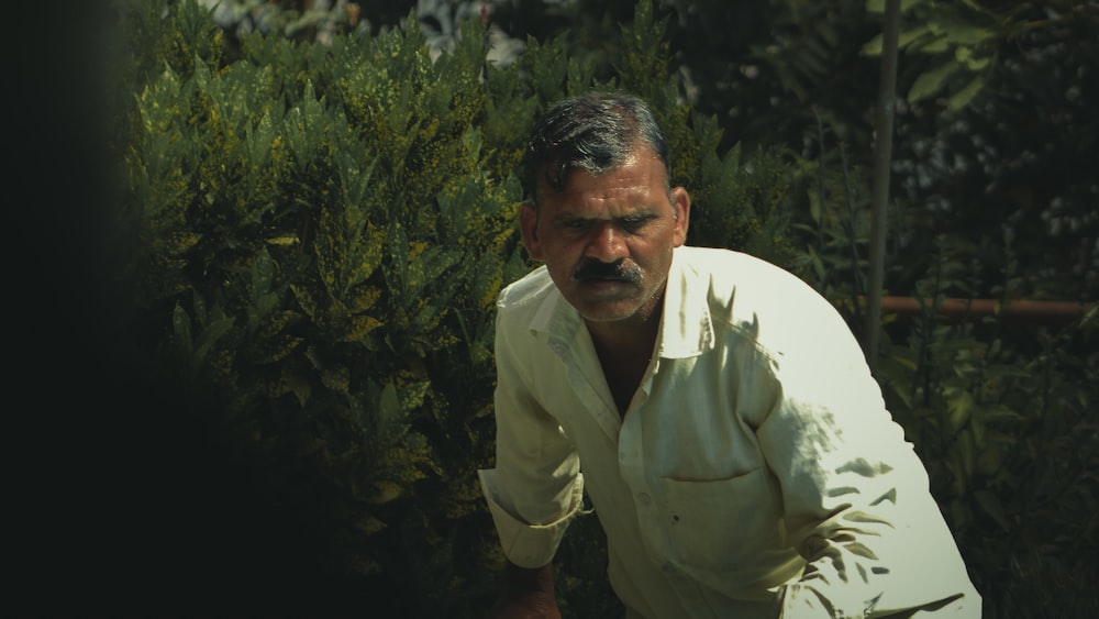 a man standing in front of a bush holding a tennis racquet