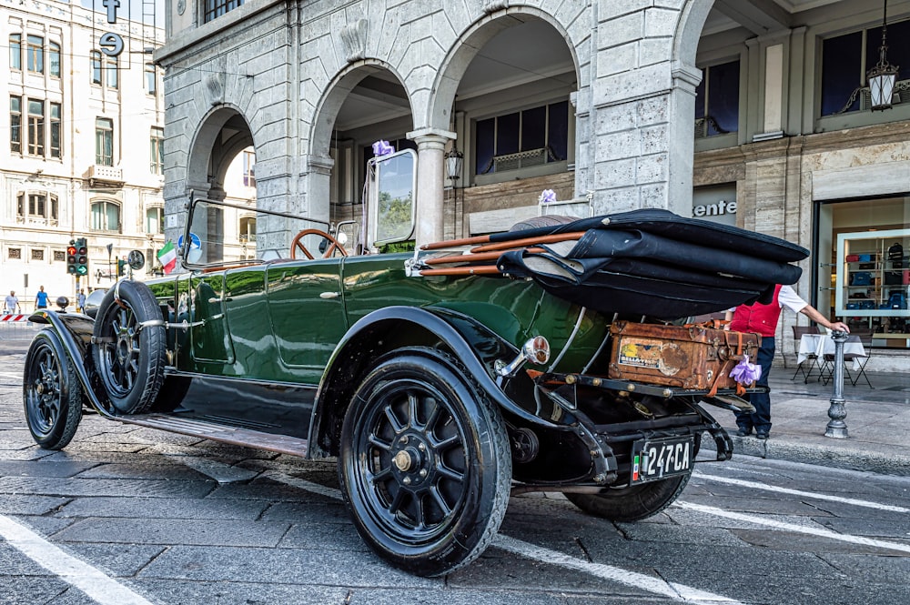 an old green car parked in front of a building