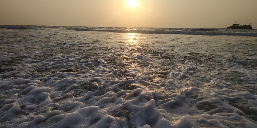 the sun is setting over the ocean with a boat in the distance