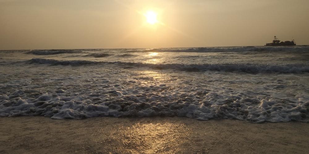 the sun is setting over the ocean with a boat in the distance