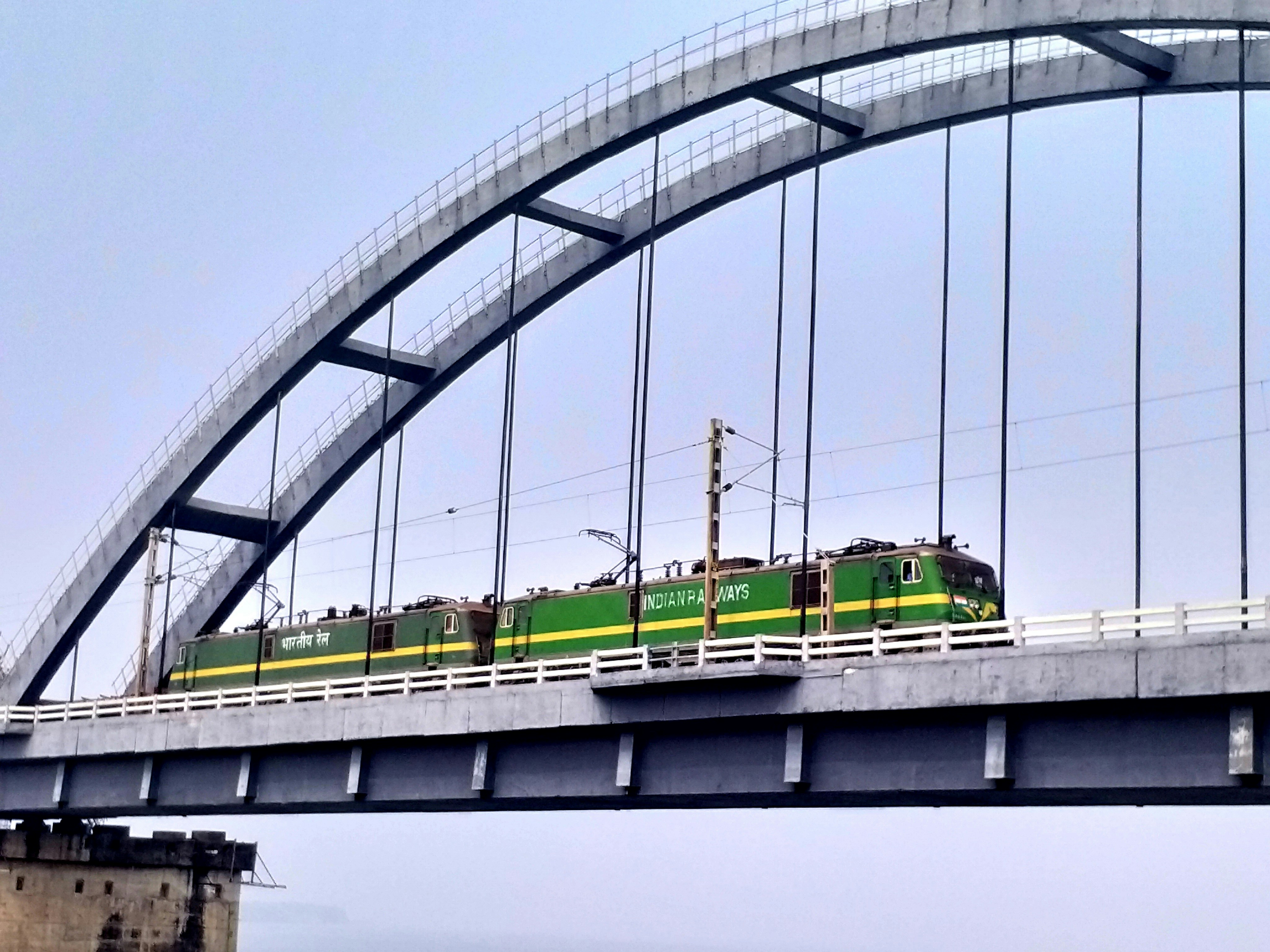 a green train traveling across a bridge over water, Indian Railways WAG 9 HH Locomotive on Rajahmundry Godavari Bridge in Andhra Pradesh. One of the powerful 9000 Horse Power freight locomotive indigenously developed by upgrading existing WAG9H, 6000HP freight locomotives capable of hauling heavier loads at higher speeds. Mostly used for Freight Service which can run at a Maximum Speed of 120 Kmph. Year of induction in service 2020 Manufacturing Unit CLW, BLW, PLW & BHEL
