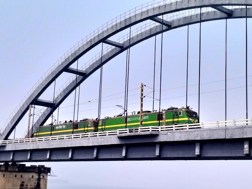 a green train traveling across a bridge over water