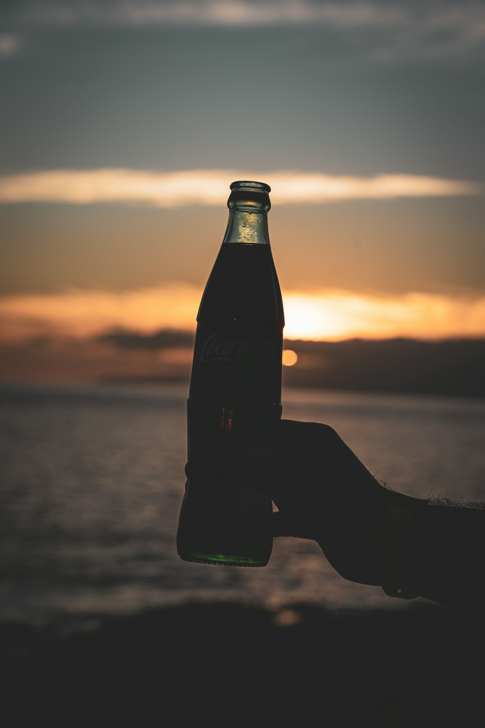 a person holding a bottle of soda in front of a sunset