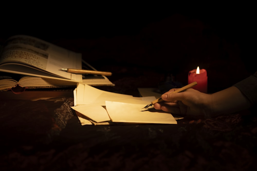 a person writing on a piece of paper next to a lit candle