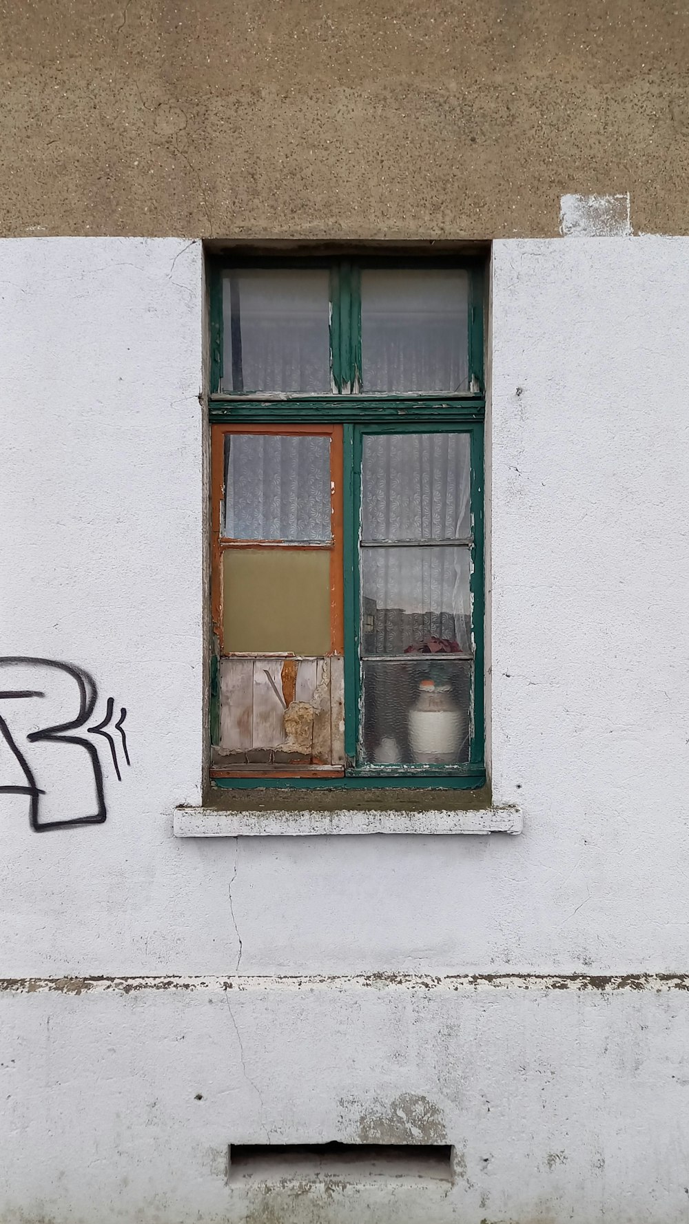 a white building with a green window and graffiti on it