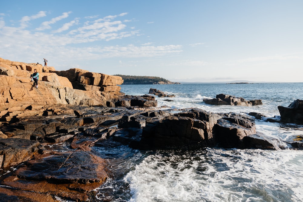 a man standing on top of a rocky cliff next to the ocean