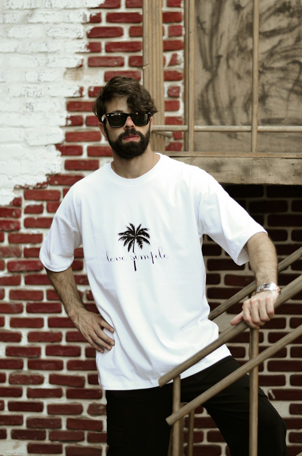 a man with a beard and sunglasses standing in front of a brick wall