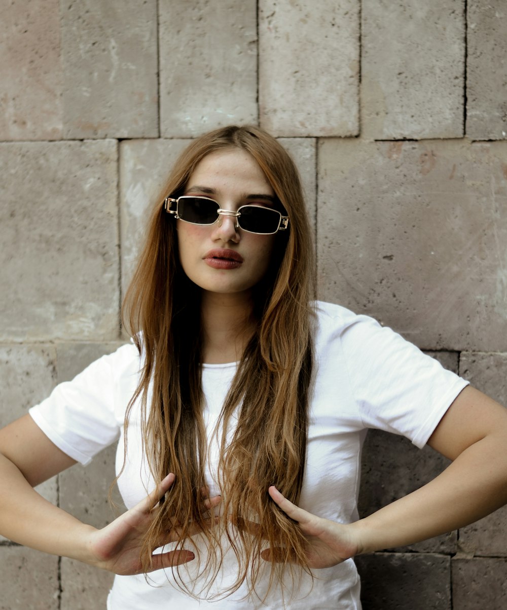 a woman wearing sunglasses standing in front of a brick wall