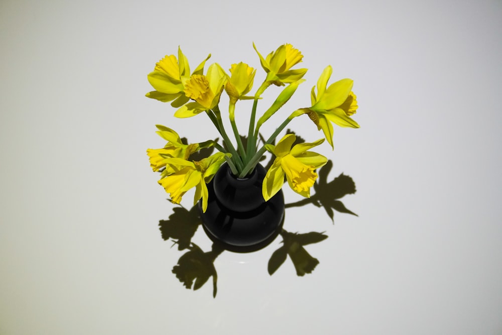 a black vase filled with yellow flowers on top of a table