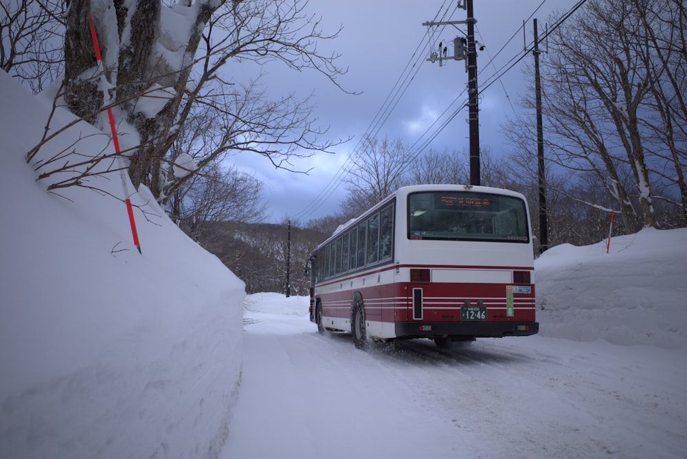 a red and white bus driving down a snow covered road