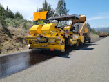 a yellow truck driving down a road next to a forest