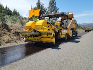 a yellow truck driving down a road next to a forest