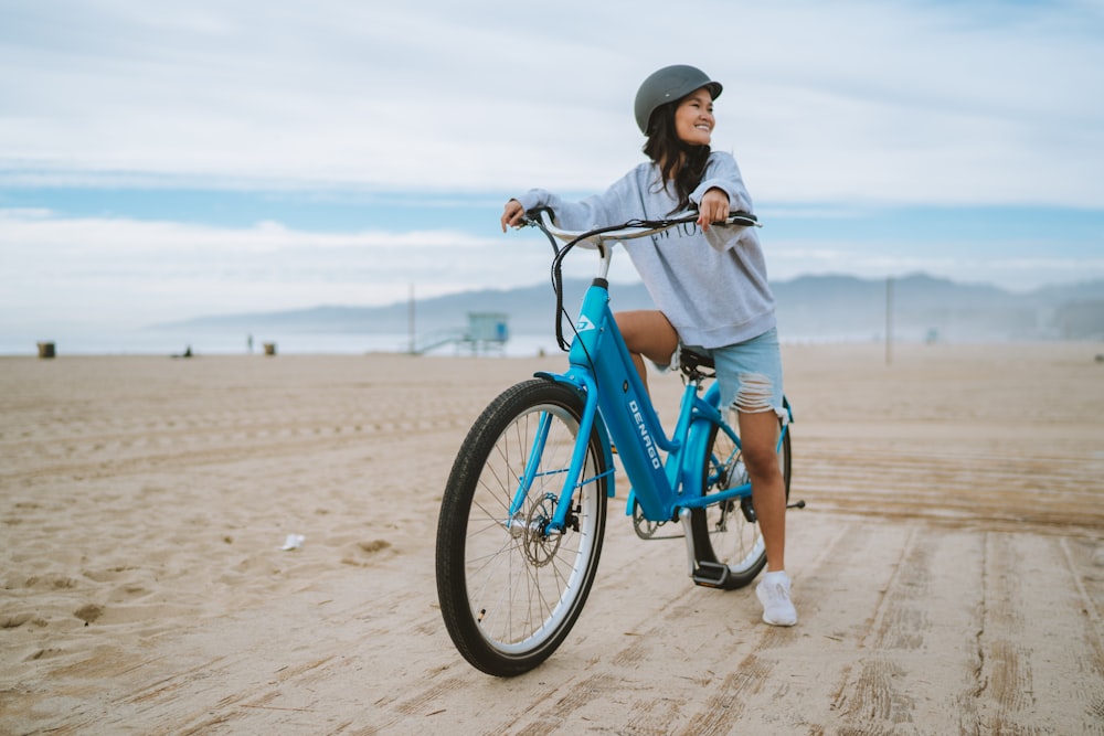 uma mulher andando de bicicleta azul em uma praia de areia