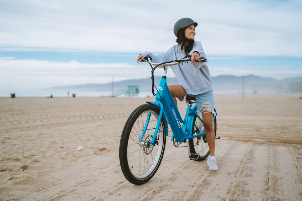 a woman riding a blue bike on a sandy beach