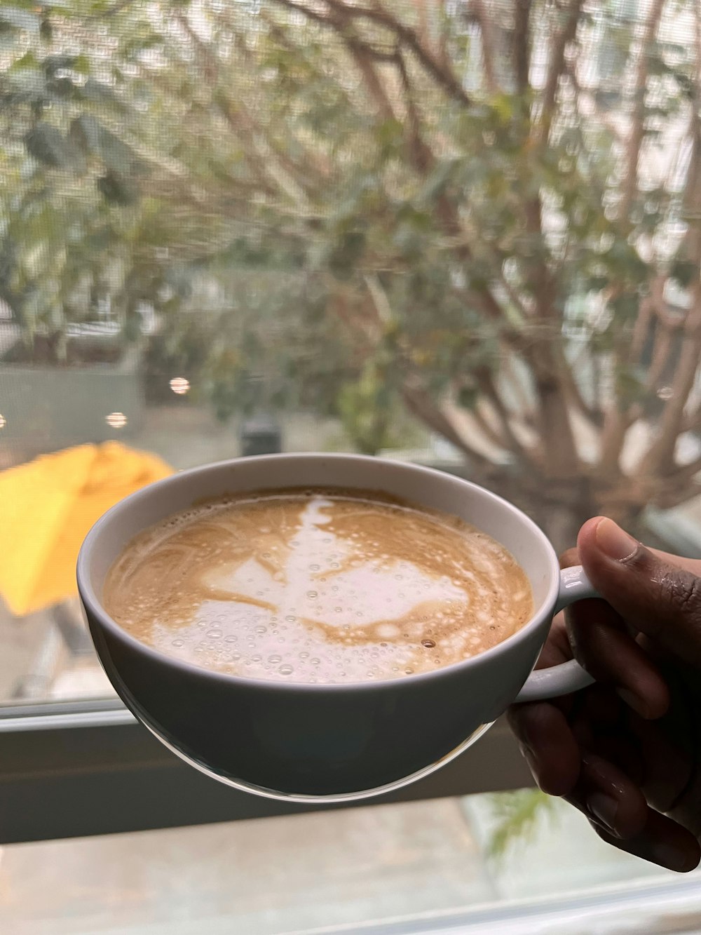 a person holding a cup of coffee in front of a window