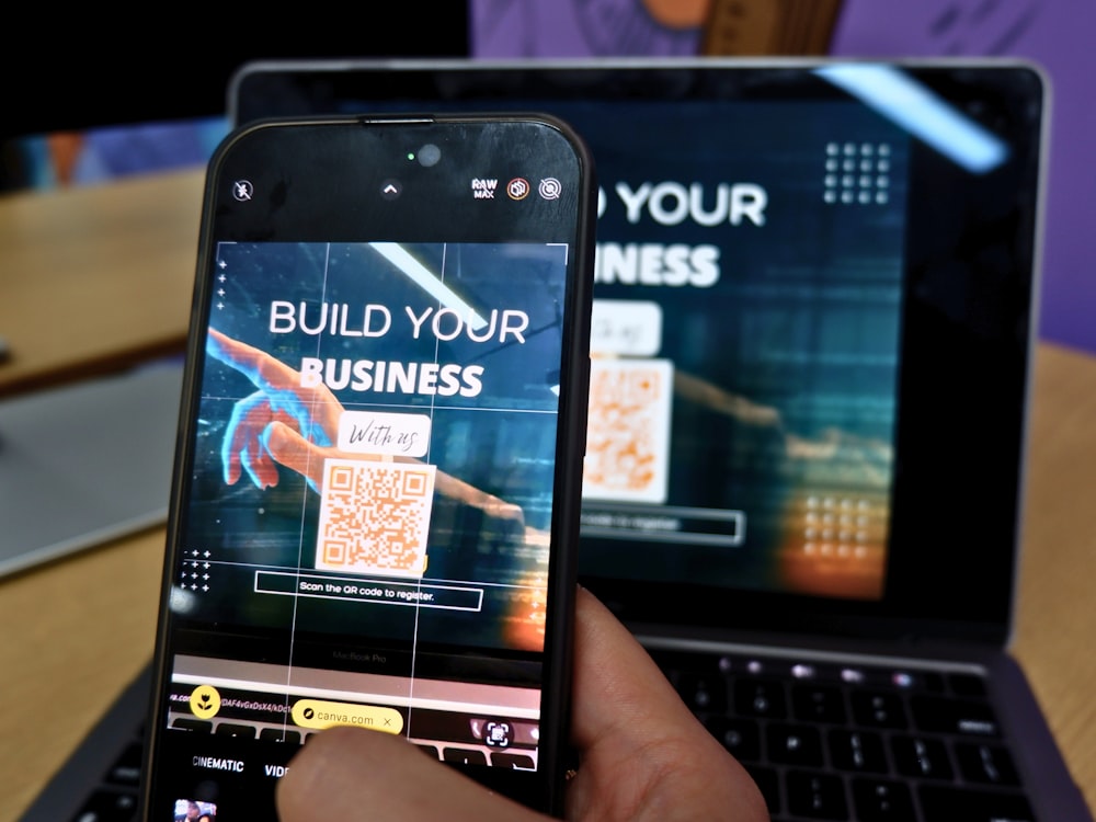 una persona sosteniendo un teléfono celular frente a una computadora portátil