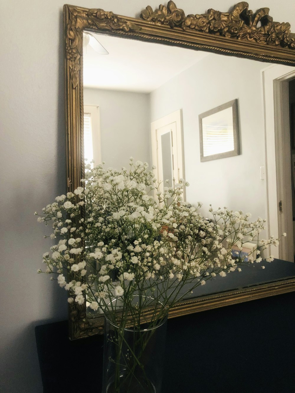 a vase filled with white flowers sitting in front of a mirror