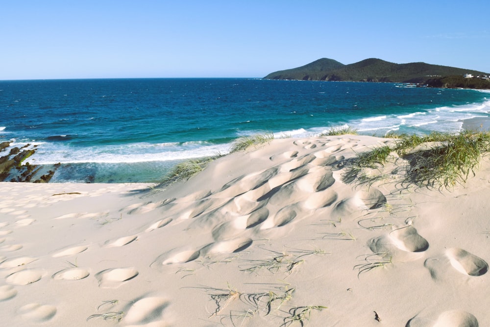 a sandy beach with blue water and hills in the background