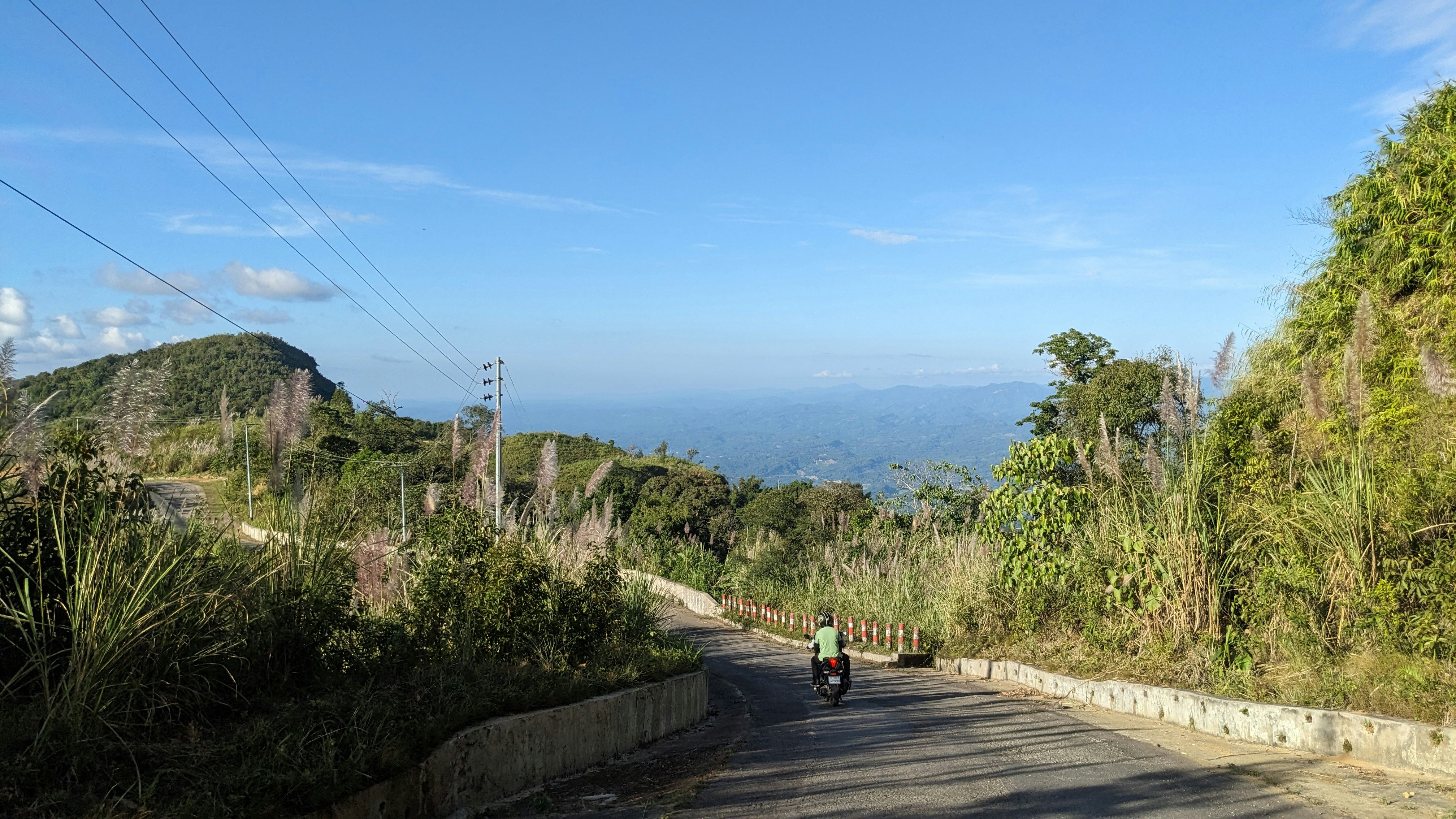 a man riding a motorcycle down a road next to a lush green hillside