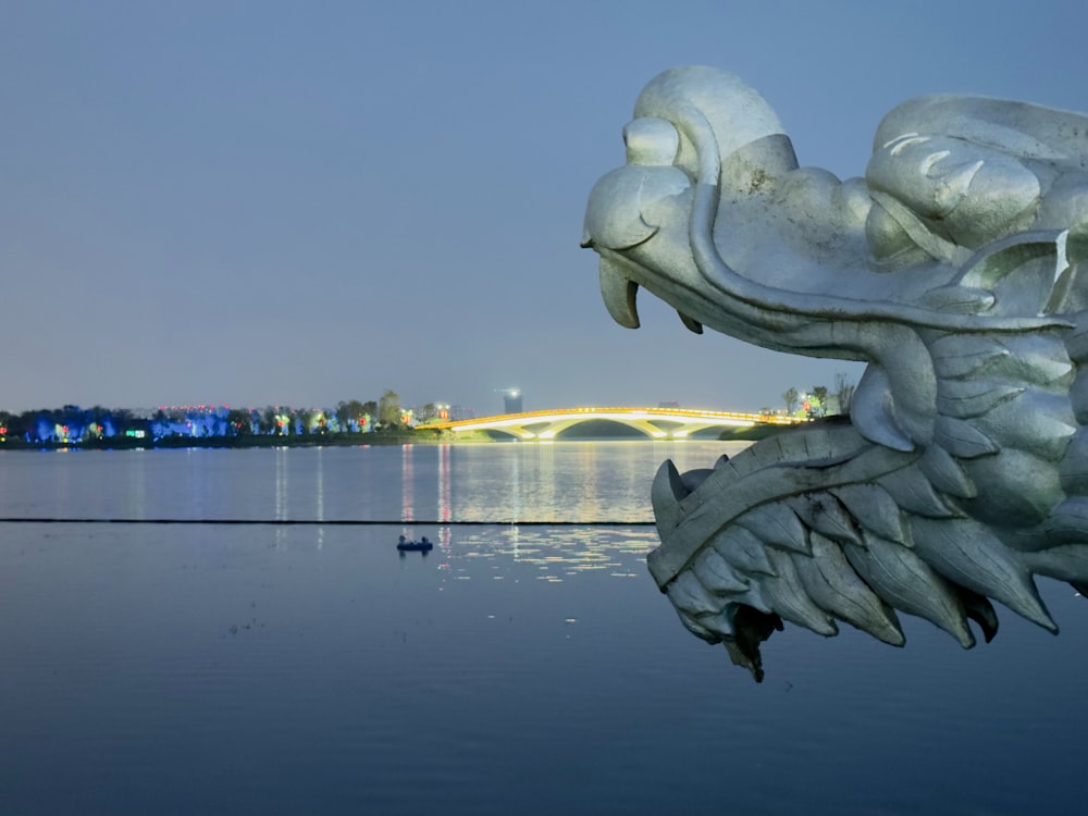 a statue of a dragon on a body of water with a bridge in the background