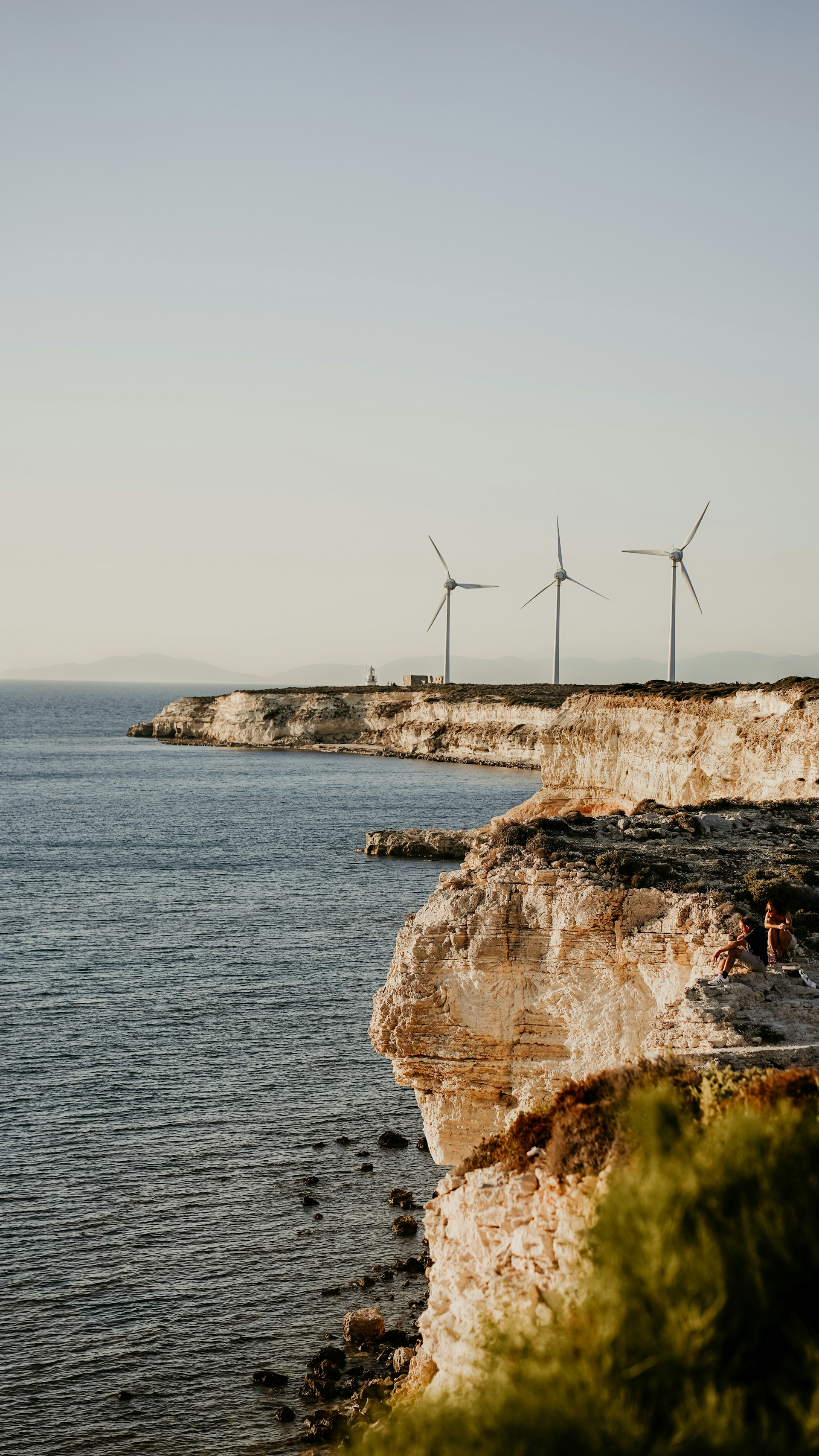 a group of people sitting on the edge of a cliff next to a body of