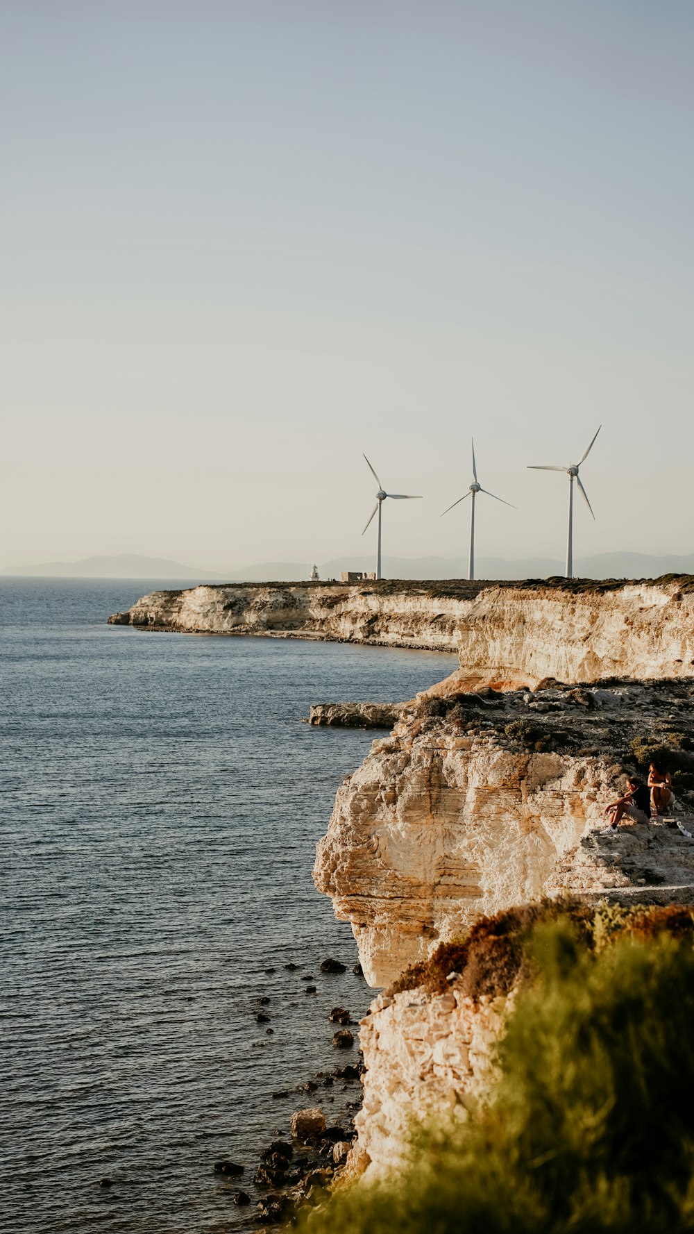 a group of people sitting on the edge of a cliff next to a body of