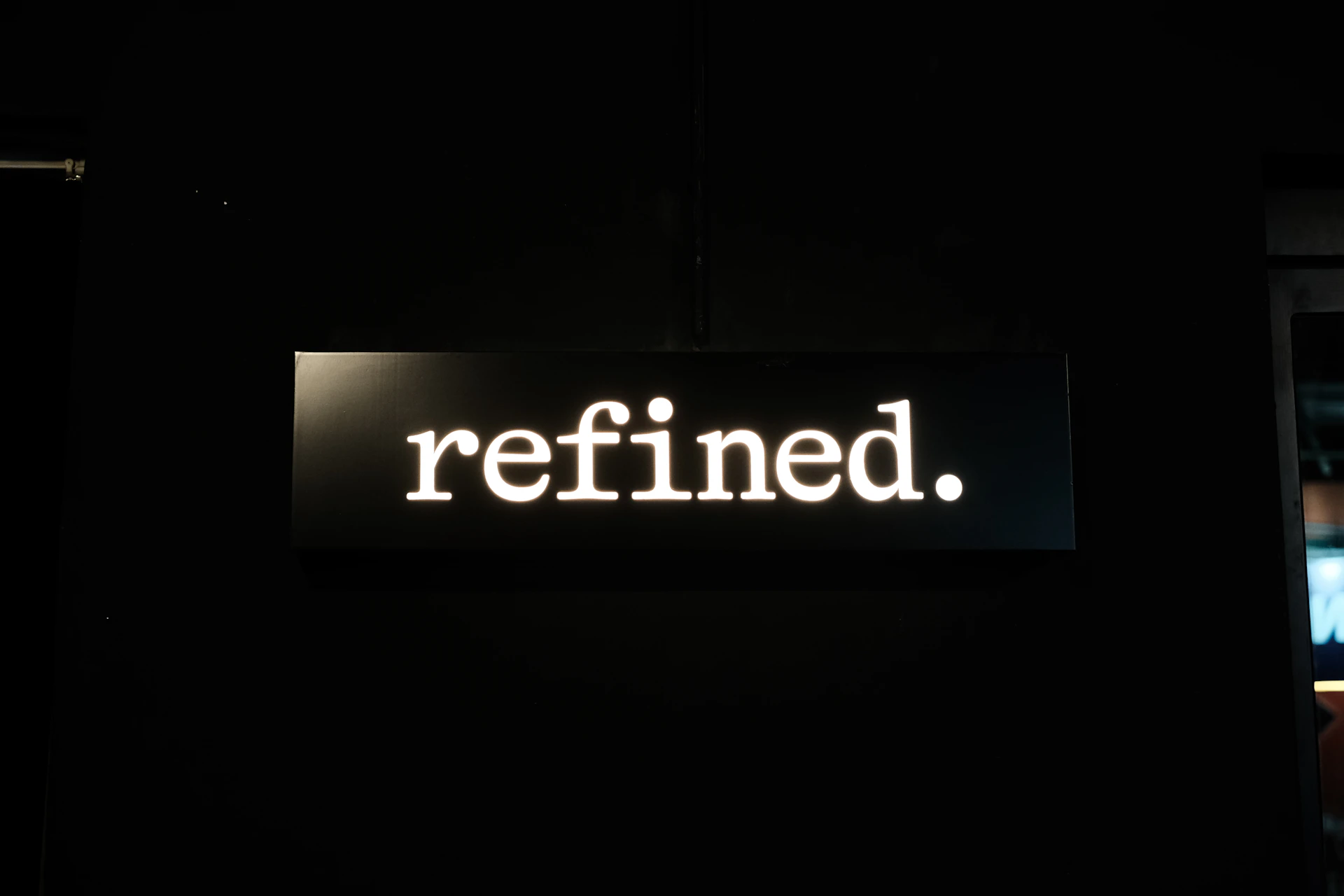 a lighted sign that says refined in a dark room