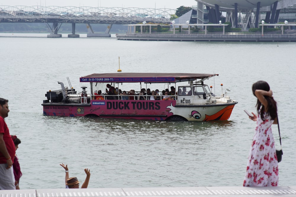 Un barco turístico rosa en el agua con un puente al fondo