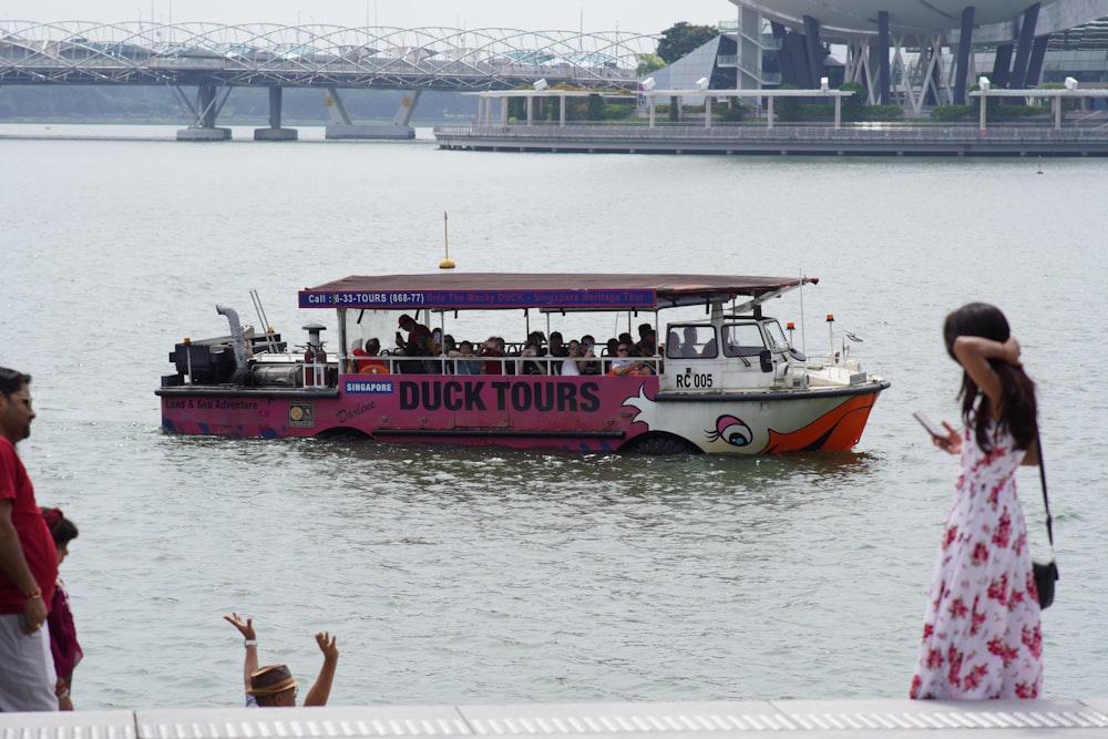 una barca da tour rosa sull'acqua con un ponte sullo sfondo