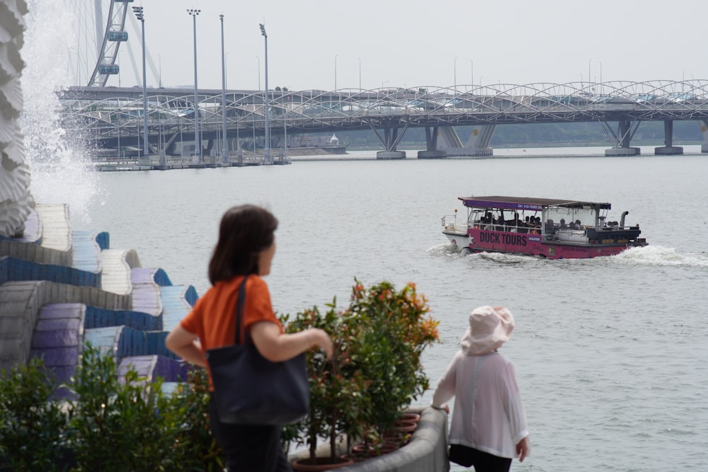 a woman and a child watching a boat go under a bridge