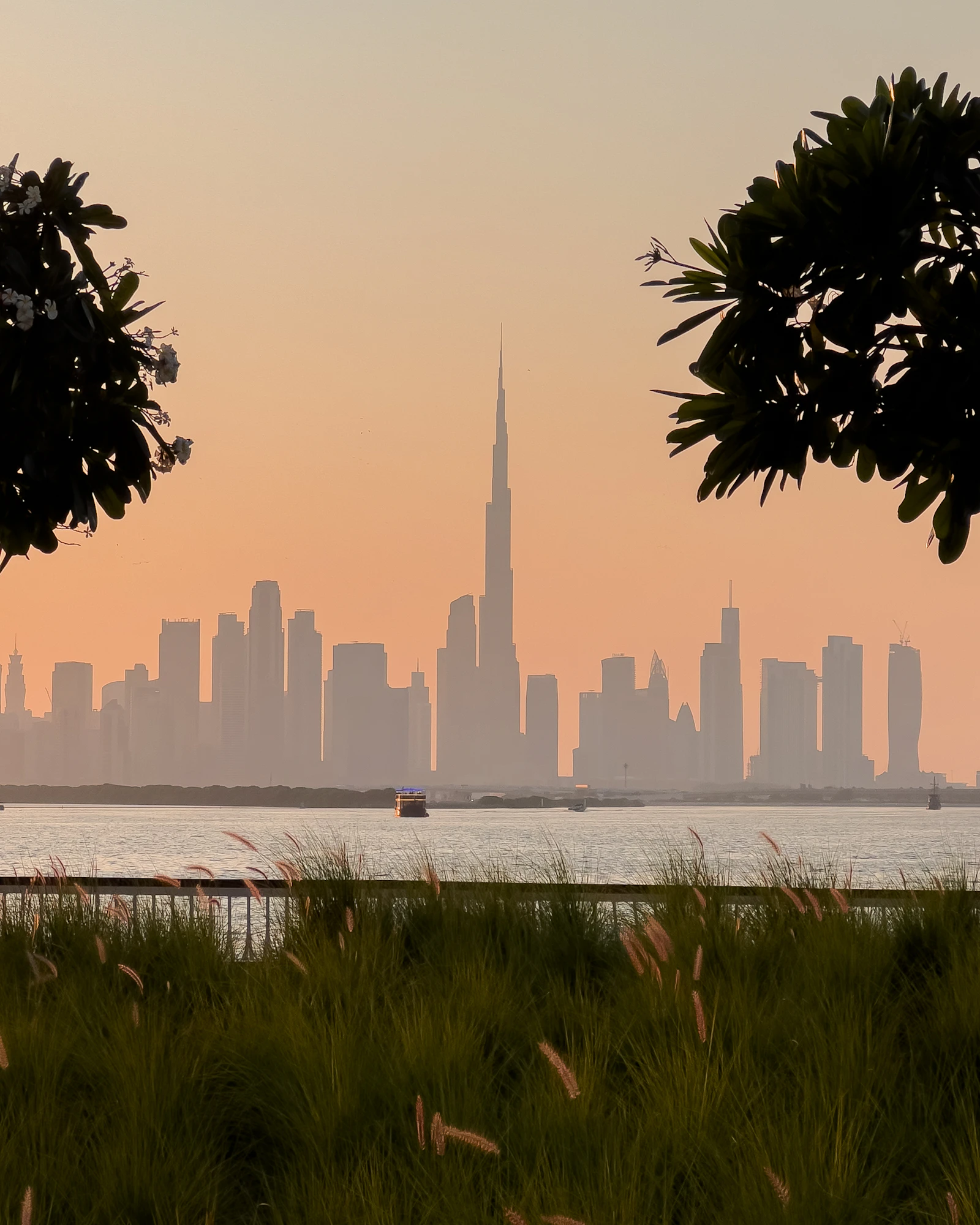 Reeds and creek-side promenade at Dubai Creek Harbour, with a boat on the creek and the Downtown skyline and Burj Khalifa across the water