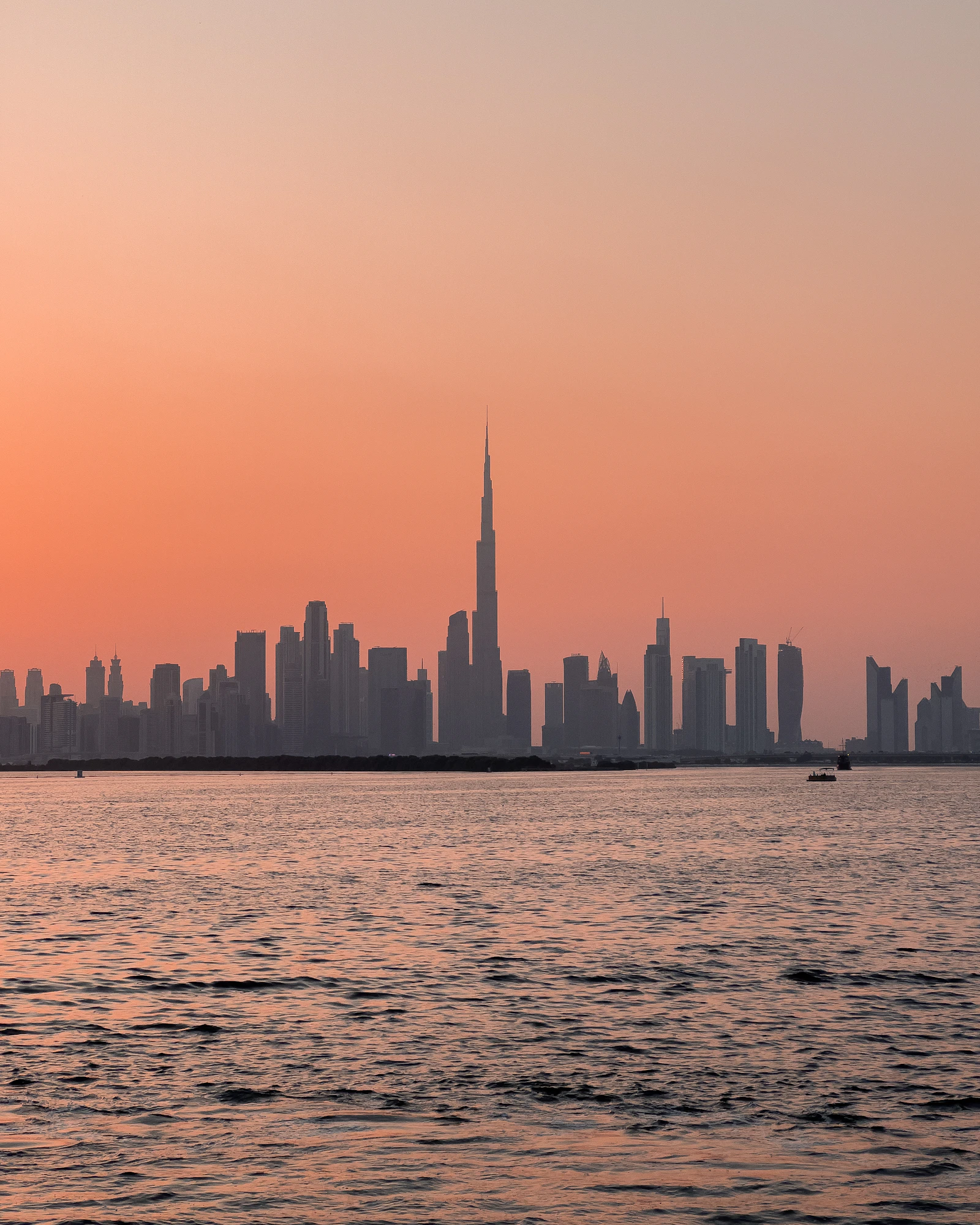 The Downtown Dubai skyline and Burj Khalifa seen across the calm creek water from Dubai Creek Harbour at dusk