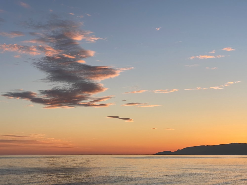 the sun is setting over the ocean with a boat in the water