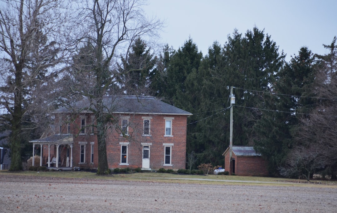 a large brick house sitting next to a forest, Historic red brick 2 story farmhouse trimmed in white with front porch