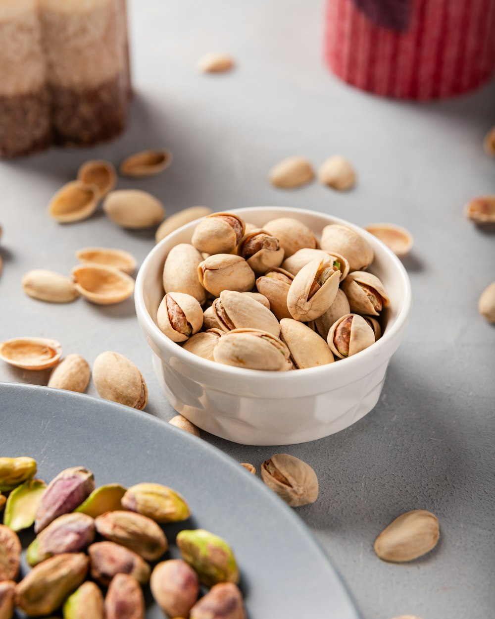 a bowl of pistachio nuts next to a plate of pistachio nuts