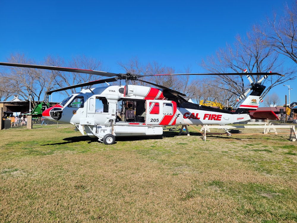 a red and white helicopter parked on top of a grass covered field
