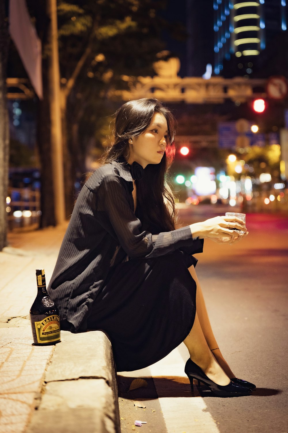 a woman sitting on a curb with a bottle of beer
