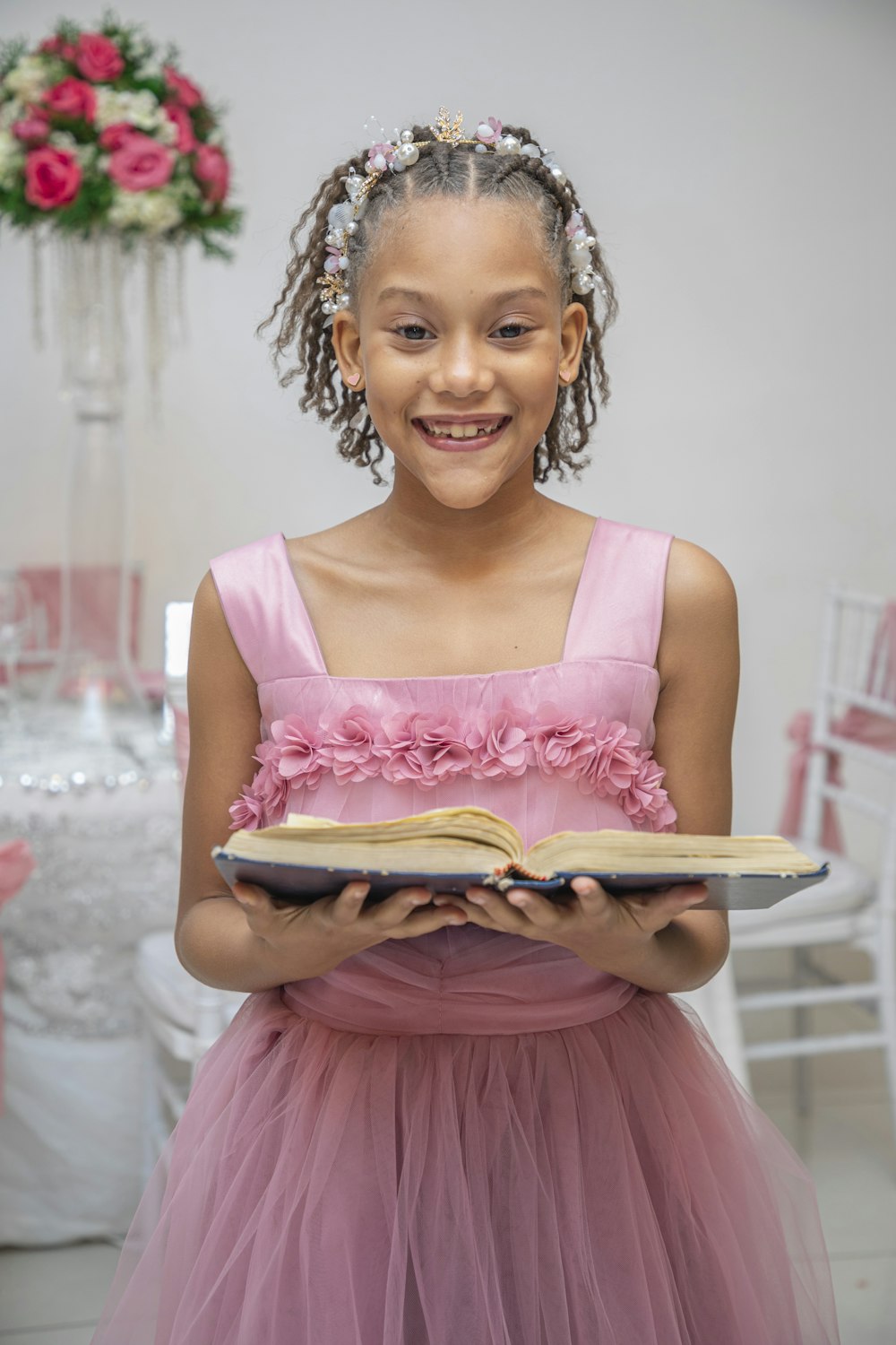 a young girl in a pink dress holding a book