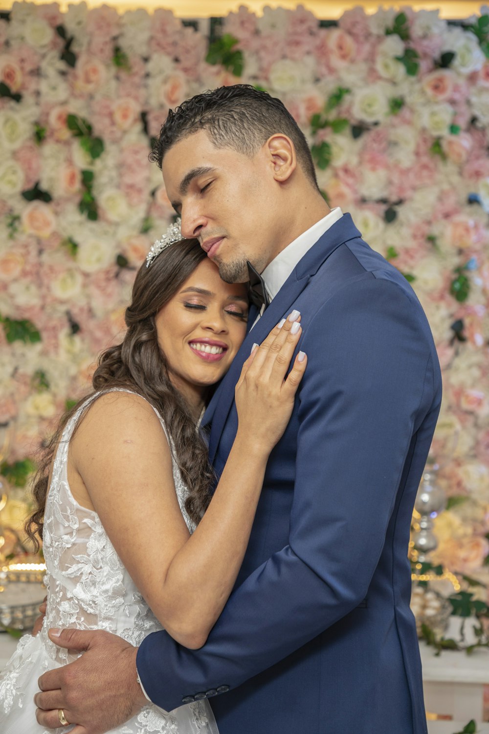 a bride and groom embracing in front of a floral wall